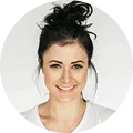 Smiling woman with dark hair tied in a messy bun wearing a white shirt, against a white background.